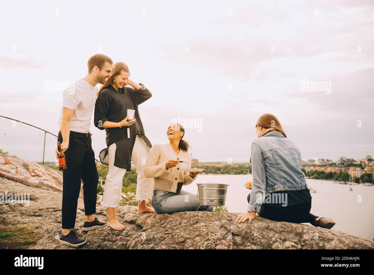 Amici felici che gustano il cibo sulla riva del lago contro il cielo Foto Stock
