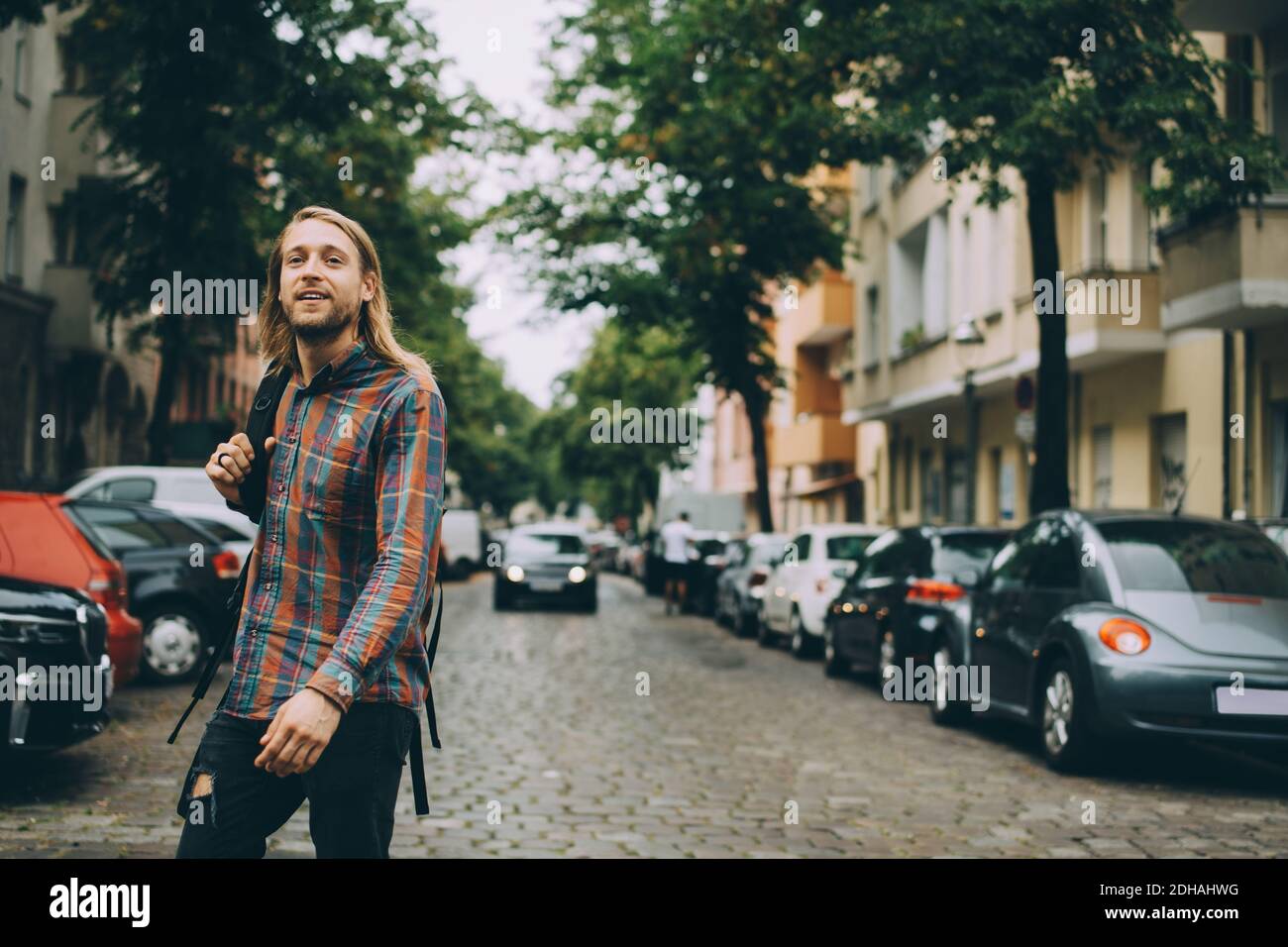 Giovane uomo che porta con sé lo zaino mentre cammina su strade acciottolate in mezzo auto in città Foto Stock