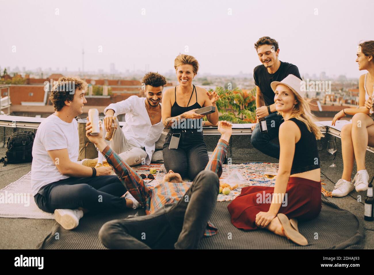 Gli amici si divertano con la musica del relatore durante la festa sul tetto in terrazza contro il cielo Foto Stock