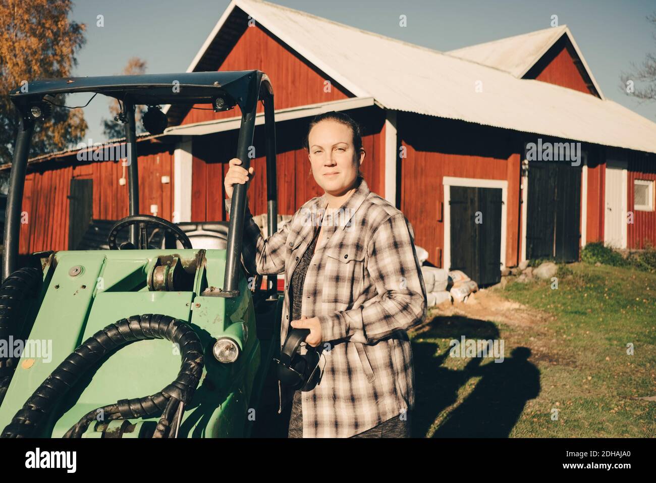 Ritratto di sicuro agricoltore in piedi da veicolo agricolo contro fienile Foto Stock