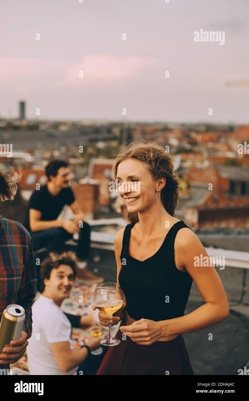 Sorrida giovane femmina gustando la birra con gli amici durante la festa sul tetto Foto Stock