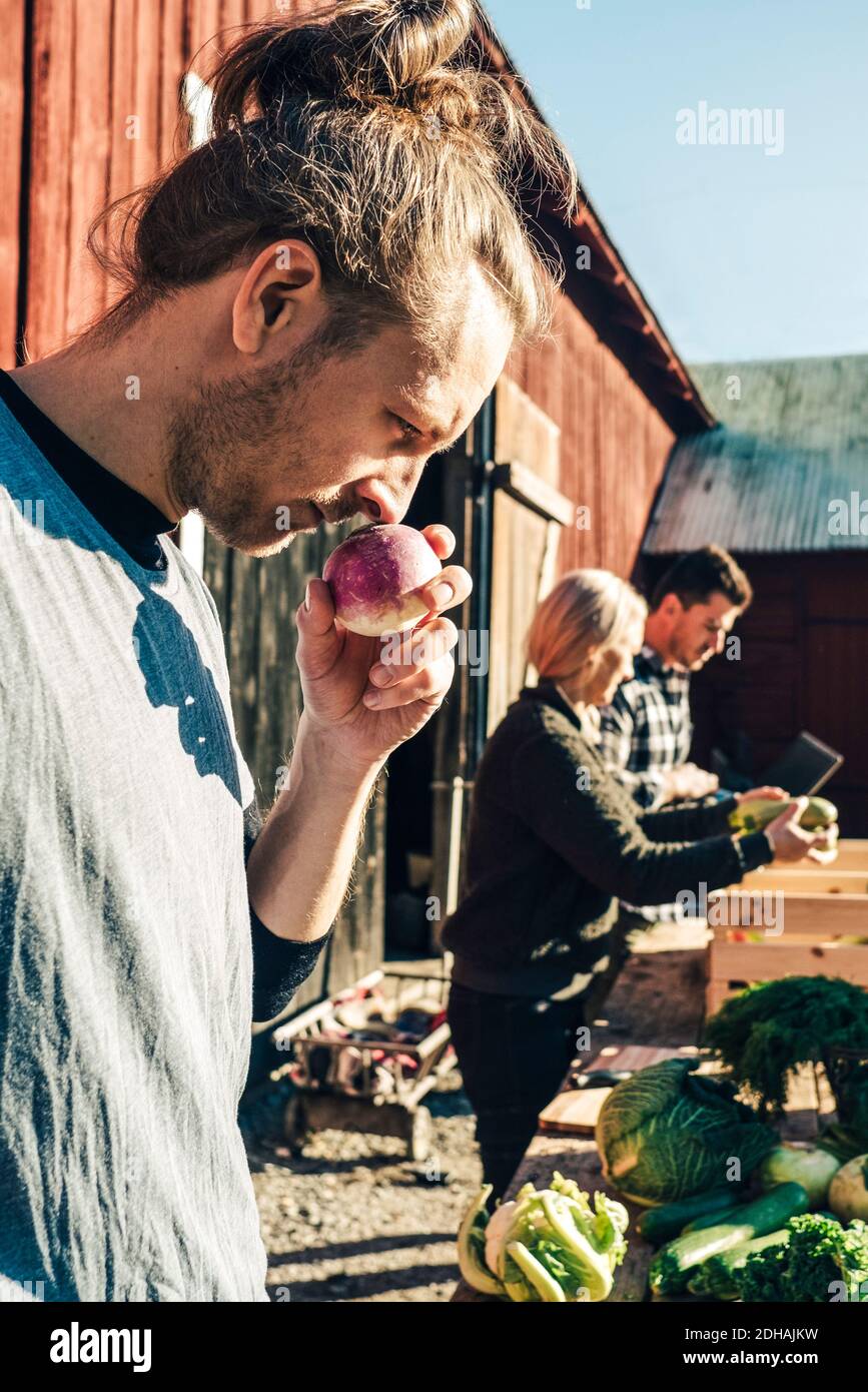 MID adulto maschio agricoltore odorare rapa con amici in background sul mercato Foto Stock