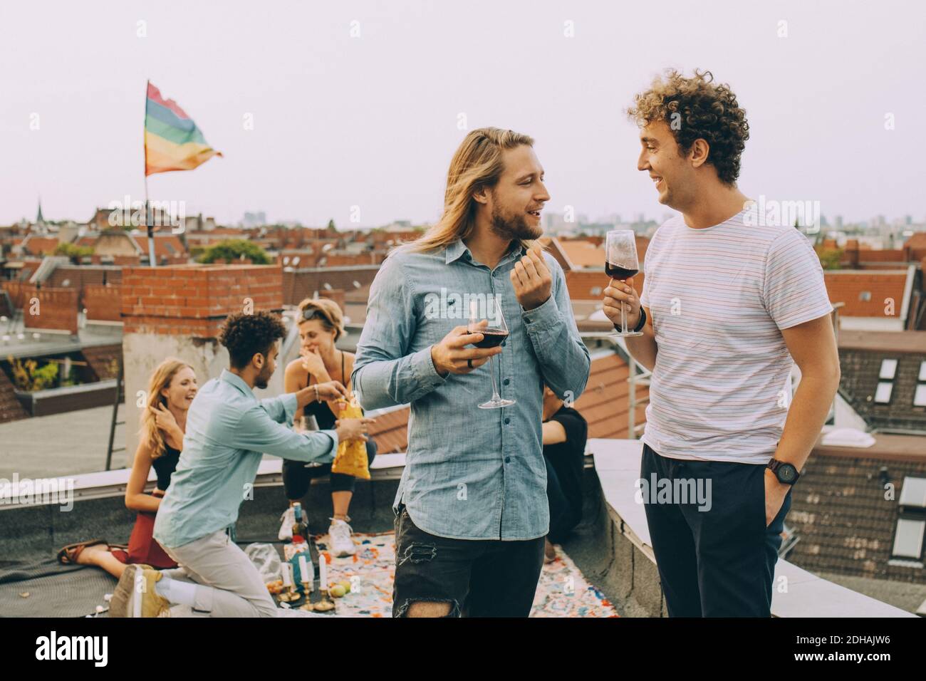 Amici che hanno vino e parlano mentre gli amici si godono sulla terrazza al party sul tetto Foto Stock