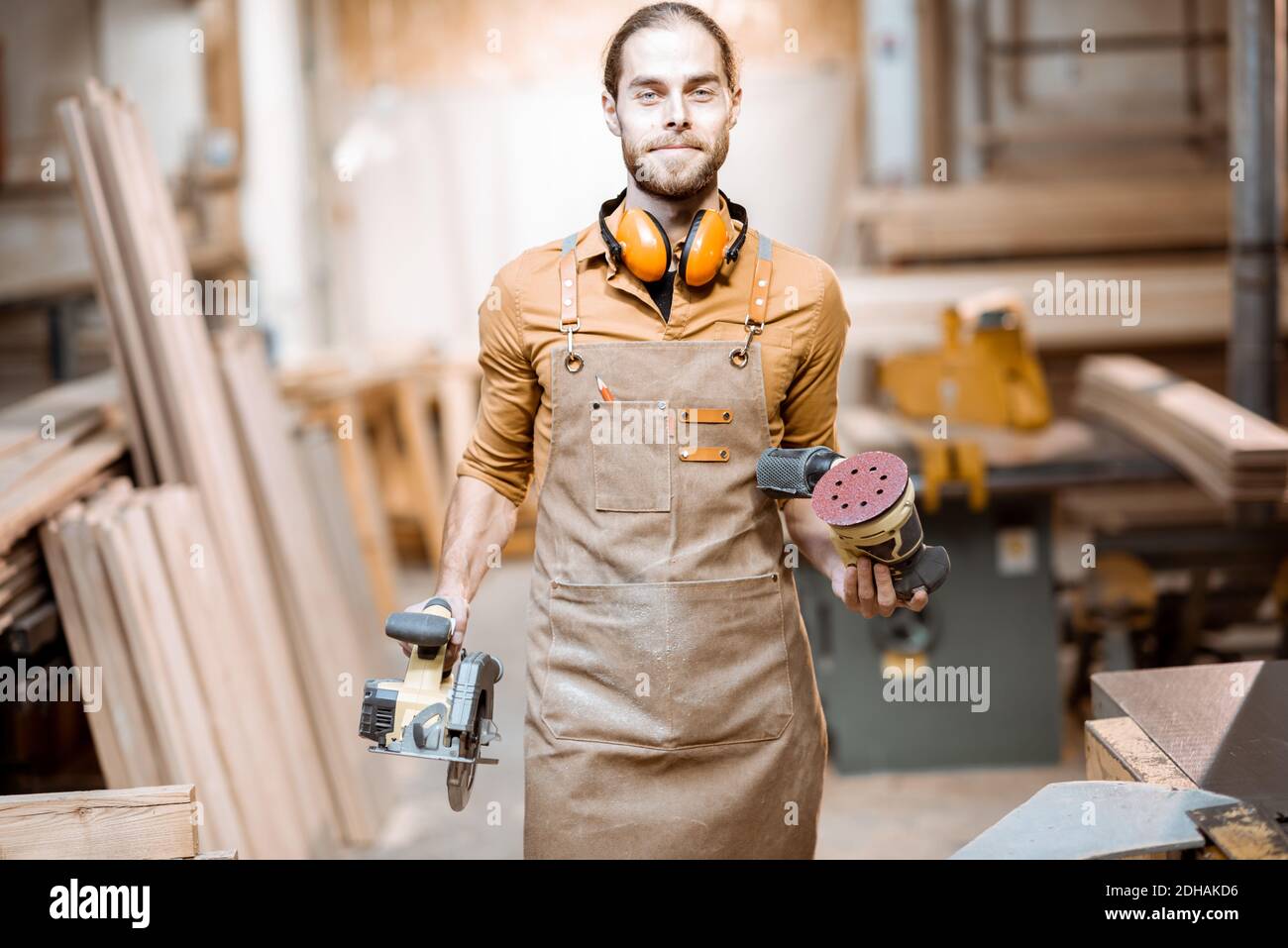 Ritratto di un bel falegname in uniforme con attrezzi moderni presso l'officina di falegnameria Foto Stock
