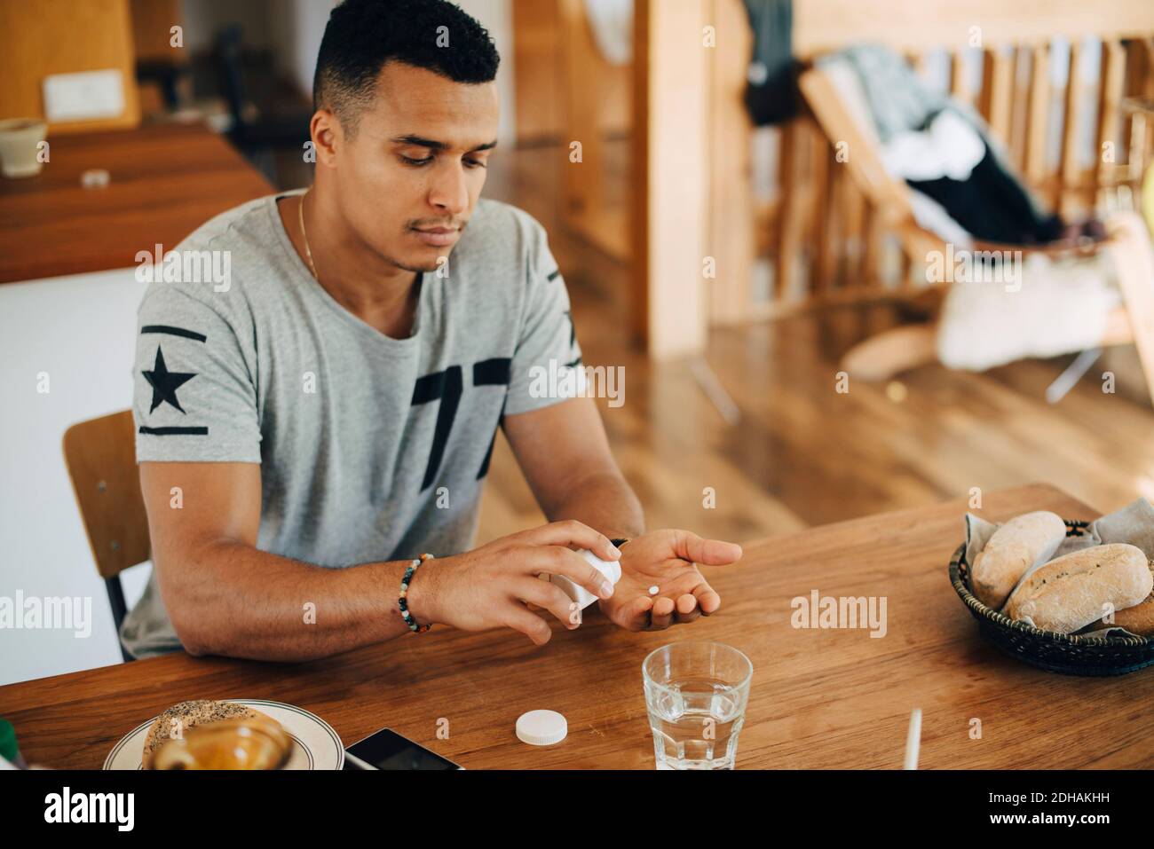 Uomo che prende le pillole mentre fa colazione al tavolo Foto Stock