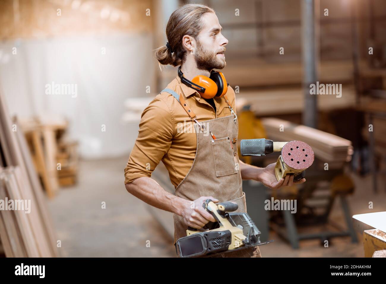 Ritratto di un bel falegname in uniforme con attrezzi moderni presso l'officina di falegnameria Foto Stock