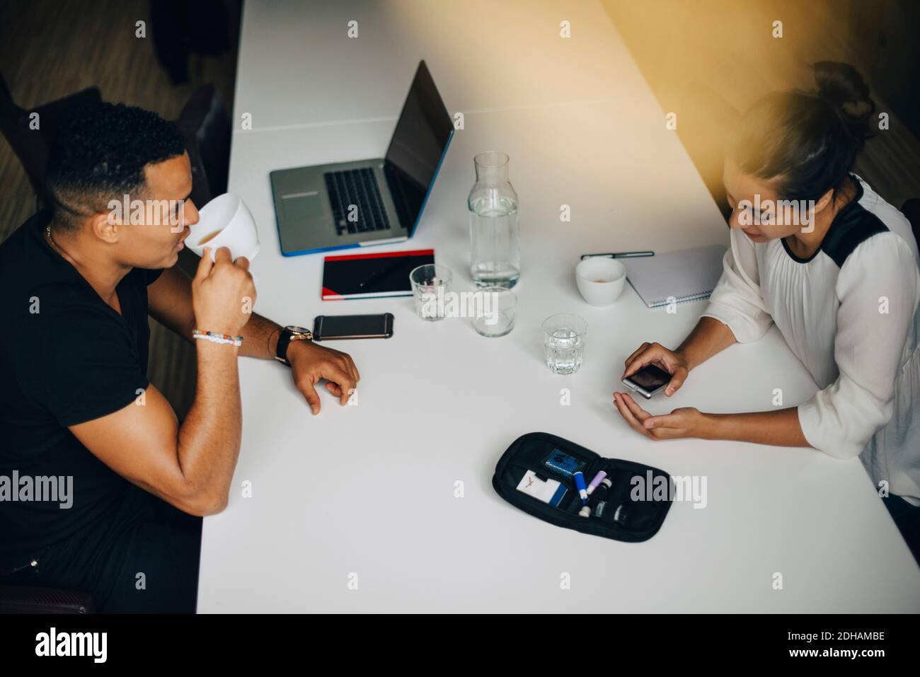 Vista ad alto angolo di una donna d'affari che fa l'esame del sangue mentre collega bere caffè al tavolo in ufficio Foto Stock