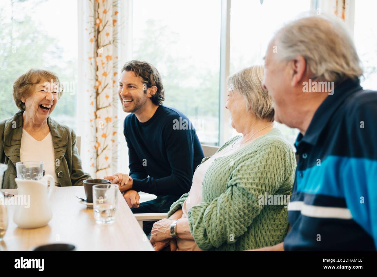Uomo sorridente che visita sua nonna e i suoi amici in pensione casa Foto Stock
