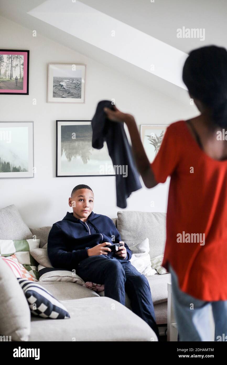 Ragazzo adolescente che guarda la madre che tiene la t-shirt in soggiorno a casa Foto Stock