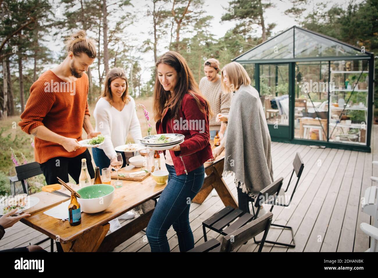 Amici di sesso maschile e femminile che portano i piatti di leftover dopo cena a. patio Foto Stock