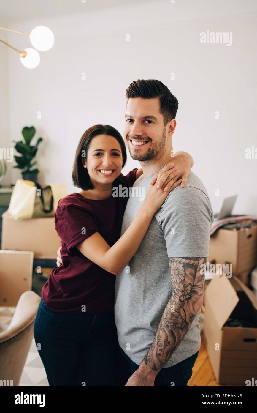 Ritratto di una coppia sorridente che si abbraccia mentre si sta in piedi in soggiorno durante il trasferimento Foto Stock