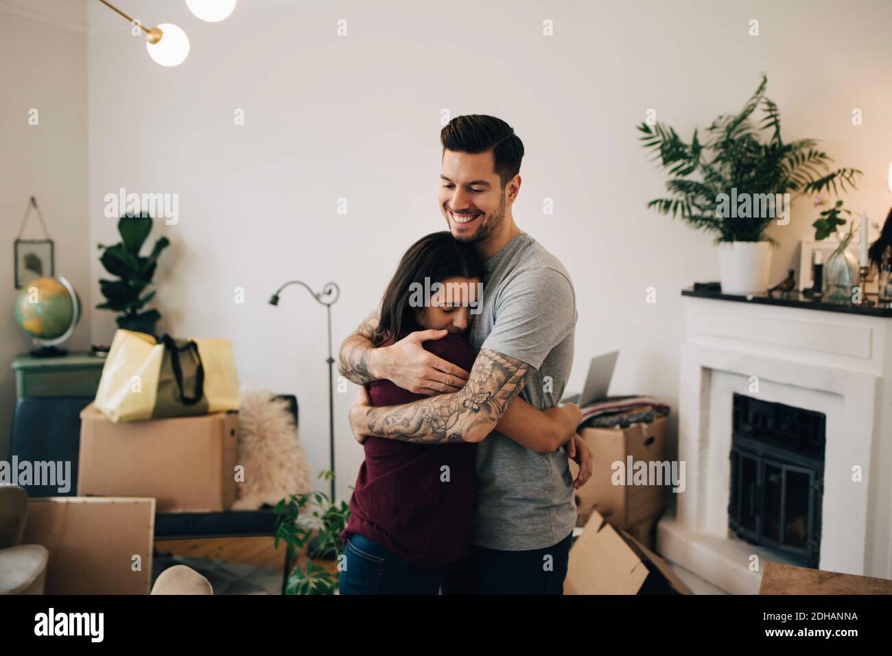 Uomo sorridente abbracciando la donna mentre si sta in salotto durante rilocazione Foto Stock