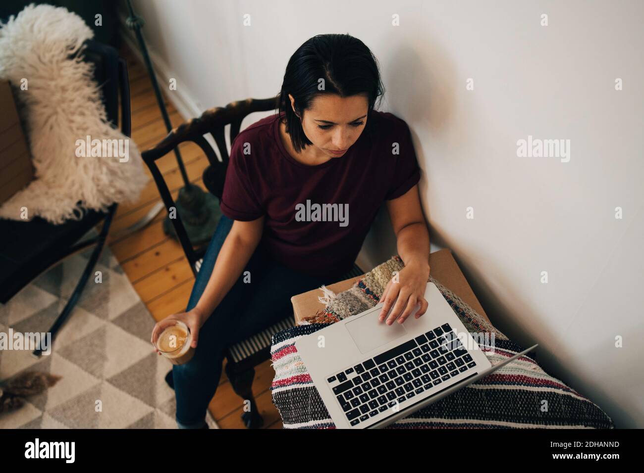 Vista ad alto angolo della donna che ha il tè mentre usa il computer portatile a parete Foto Stock