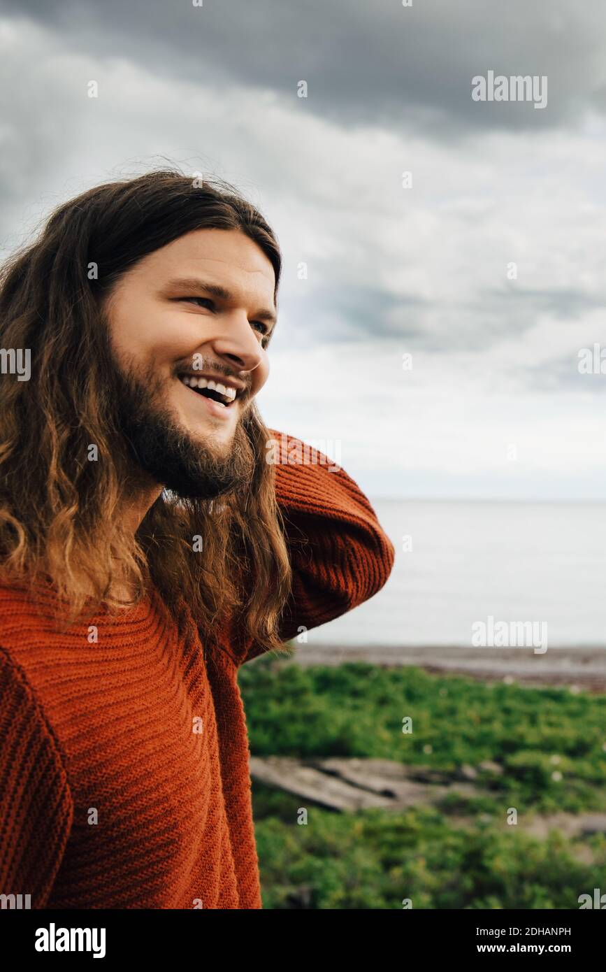 Primo piano di uomo sorridente con capelli lunghi contro la spiaggia Foto Stock