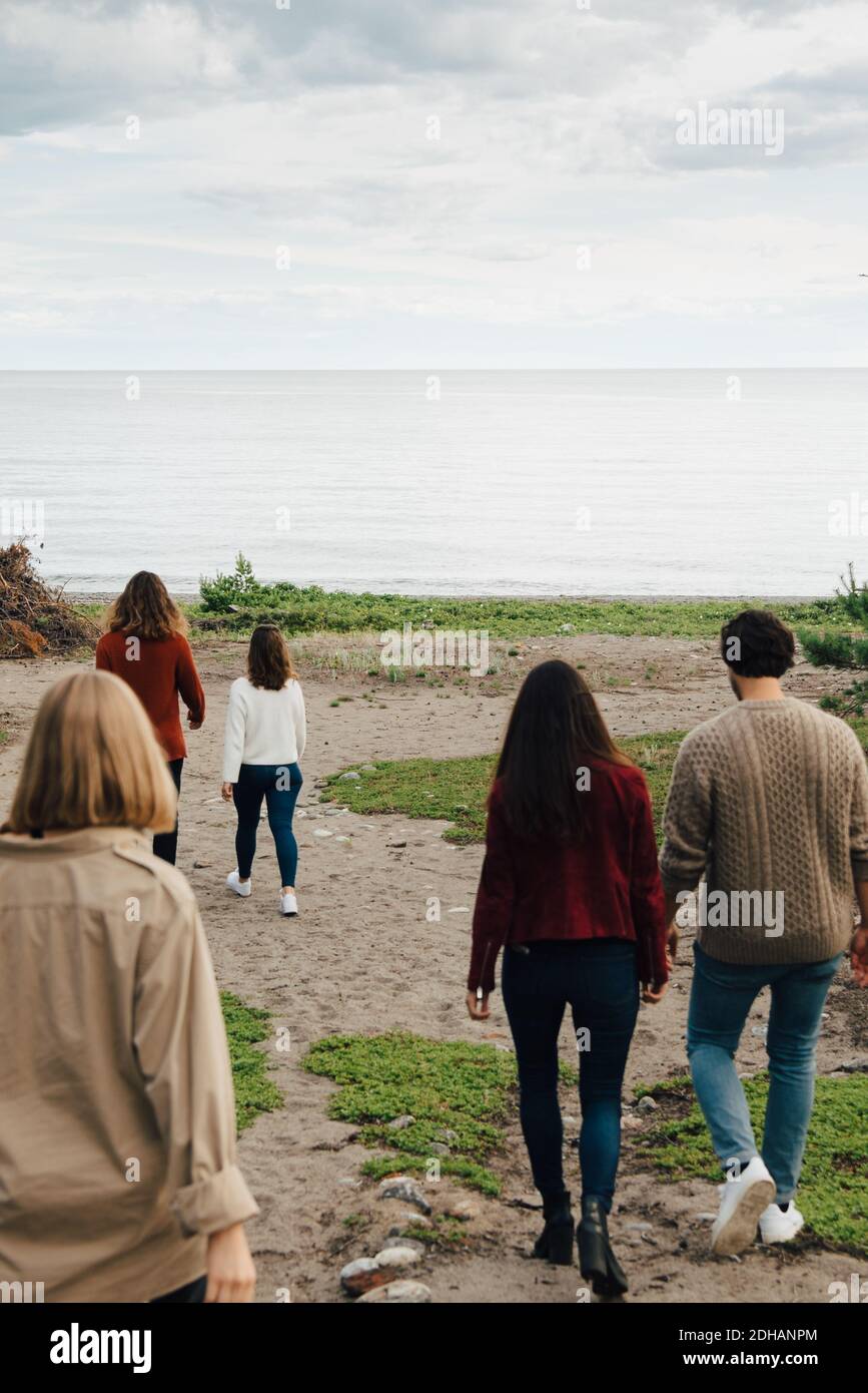Vista posteriore degli amici che camminano verso il mare contro il cielo Foto Stock