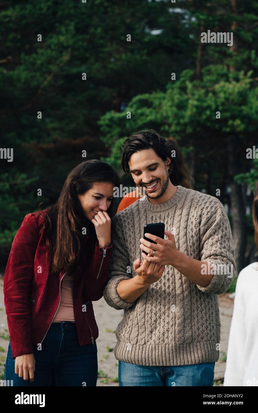 Uomo sorridente che mostra lo smartphone ad un amico mentre si godono le vacanze Foto Stock