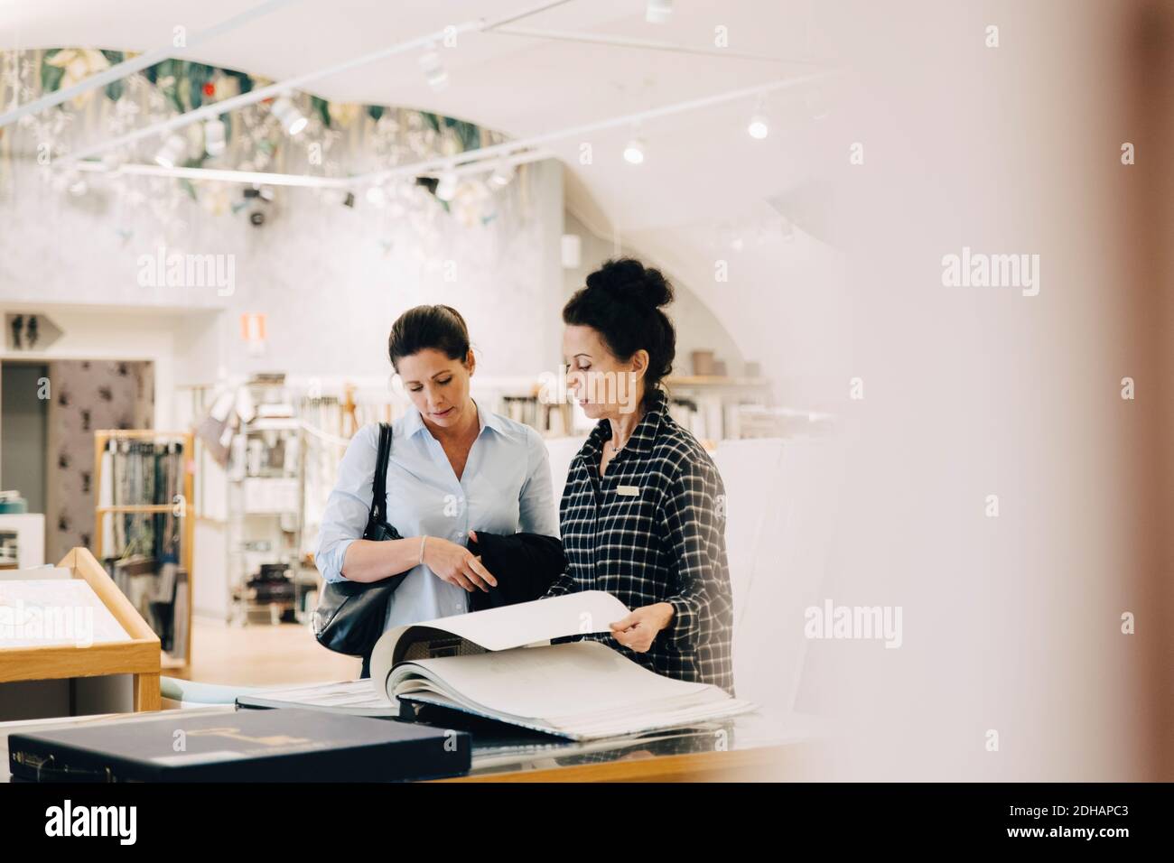 Venditore che assiste il cliente femminile nella scelta del campione di carta da parati in negozio Foto Stock