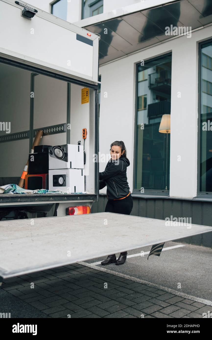 Lavoratore femminile apertura tronco di furgone di consegna in città Foto Stock