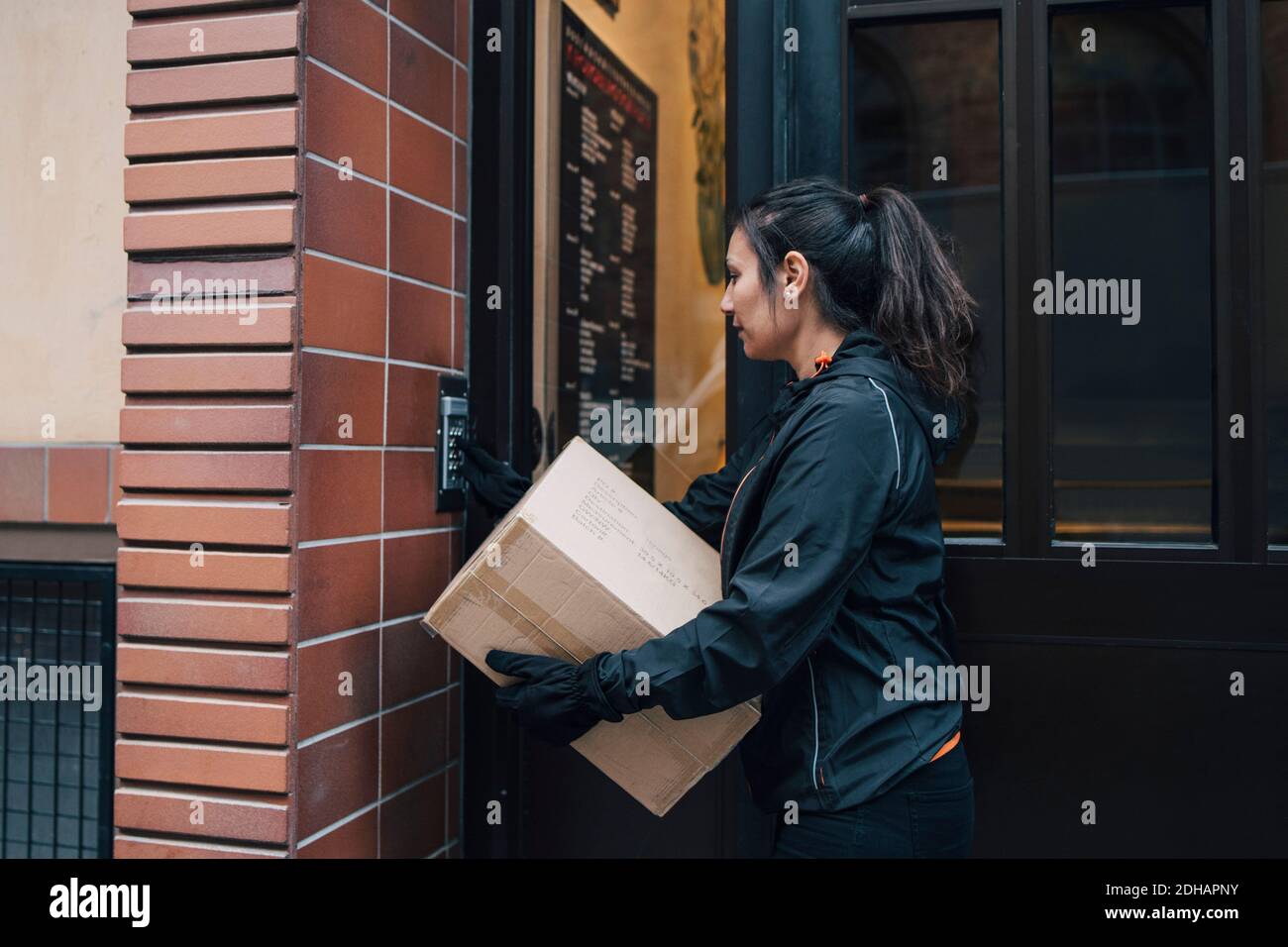 Citofono a suoneria Messenger femminile mentre si porta la scatola chiusa Foto Stock