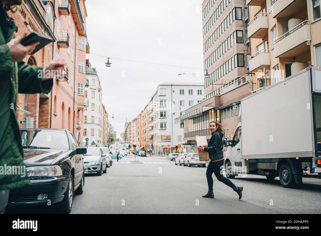 Donna che corre con un furgone di consegna mentre si trasporta la scatola in città contro il cielo limpido Foto Stock