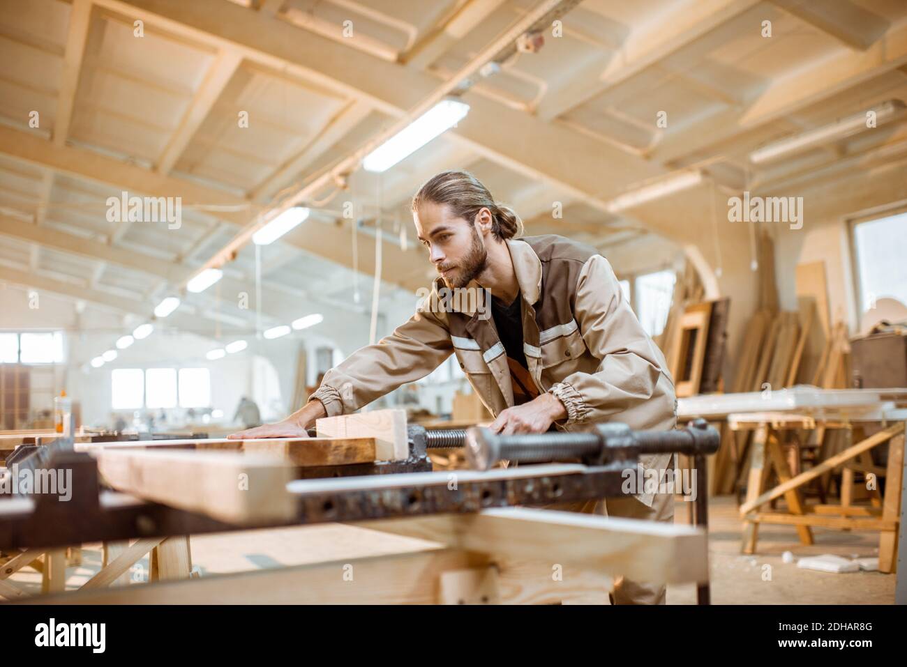 Bel falegname in uniforme incollaggio di barre di legno con pressioni a mano alla produzione di carpenteria Foto Stock