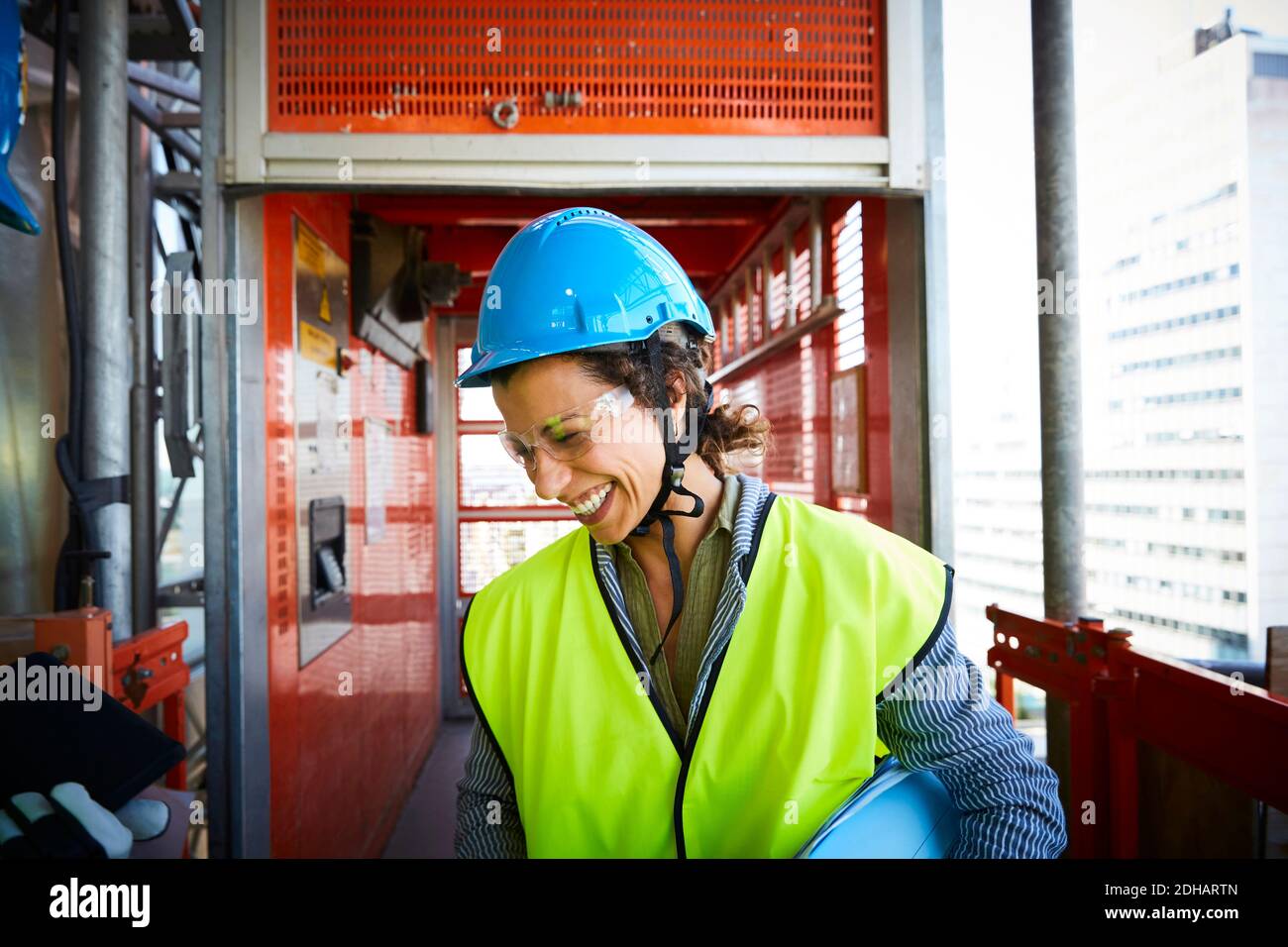 Sorridente ingegnere femminile in abiti riflettenti in cantiere Foto Stock