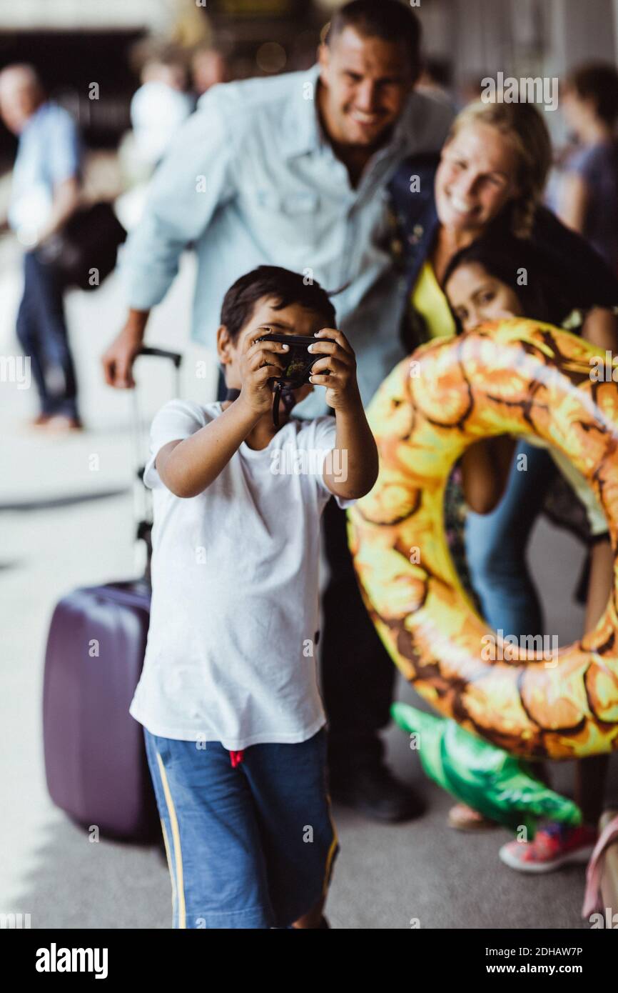 Ragazzo che prende selfie con la famiglia sulla macchina fotografica alla stazione ferroviaria durante le vacanze Foto Stock
