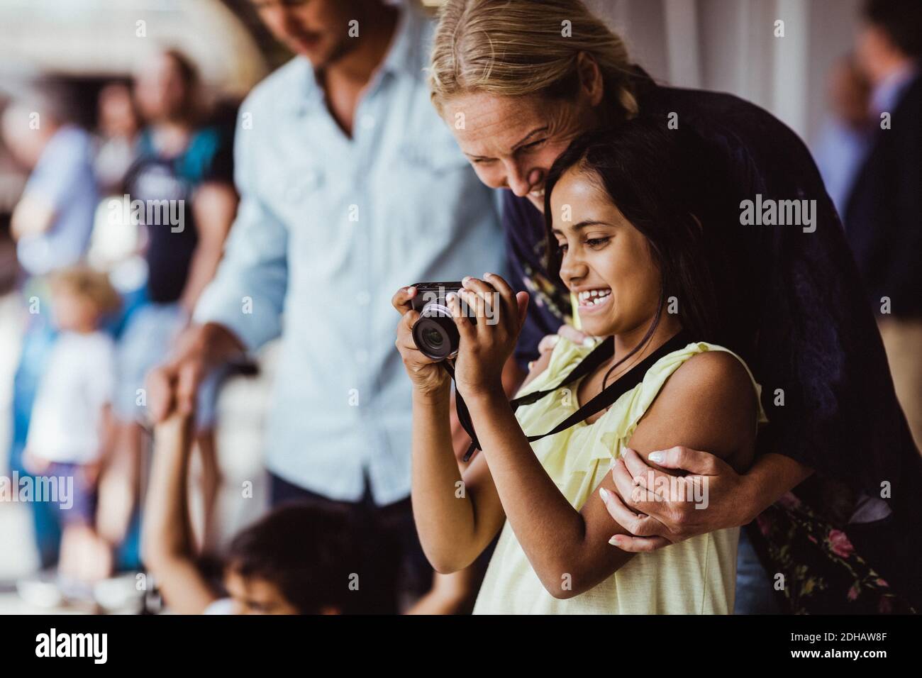 Felice figlia che mostra la macchina fotografica alla madre mentre sta in piedi dalla famiglia alla stazione Foto Stock