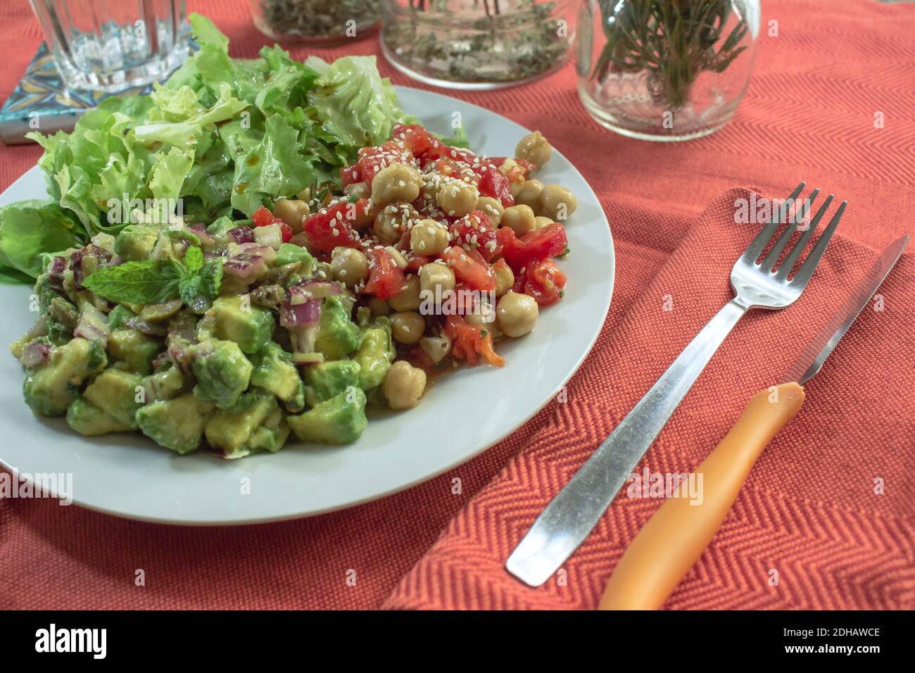 Un tavolo con tovaglia rossa e un piatto vegano con insalata di ceci e pomodoro, insalata di avocado e lattuga Foto Stock