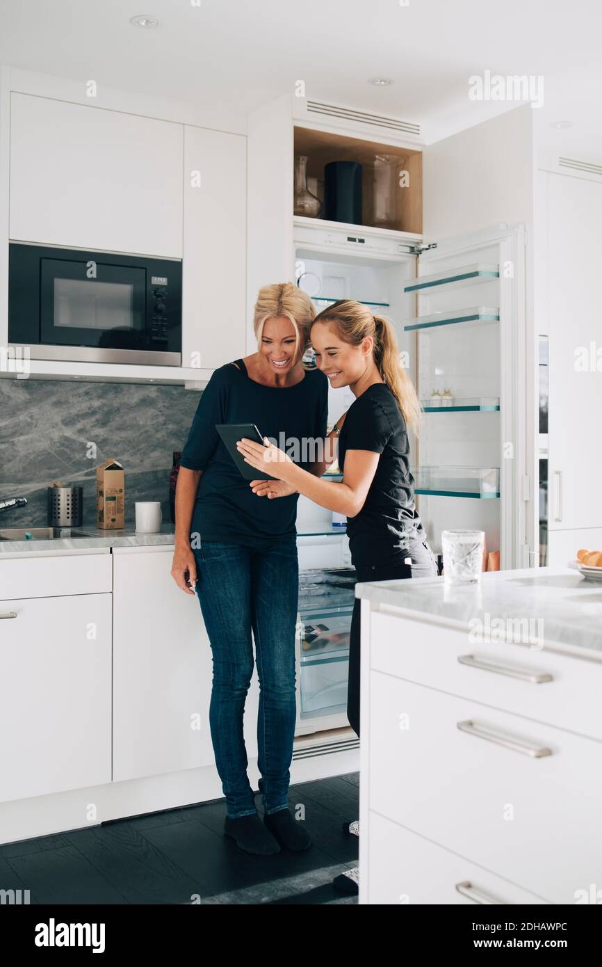 Allegra ragazza adolescente che condivide il tablet digitale con la madre in cucina a casa Foto Stock