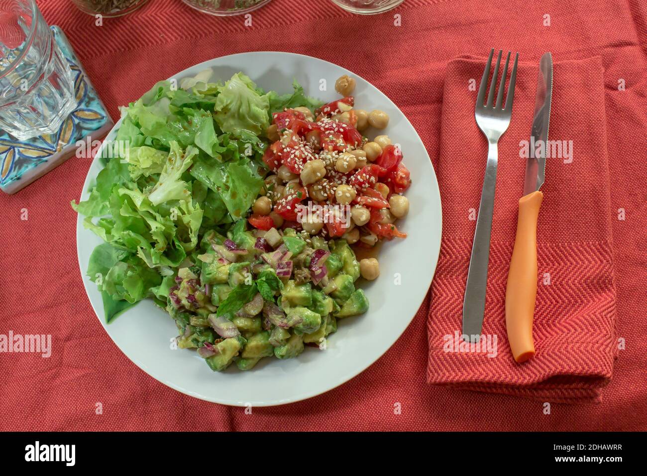 Un tavolo con tovaglia rossa e un piatto vegano con insalata di ceci e pomodoro, insalata di avocado e lattuga Foto Stock