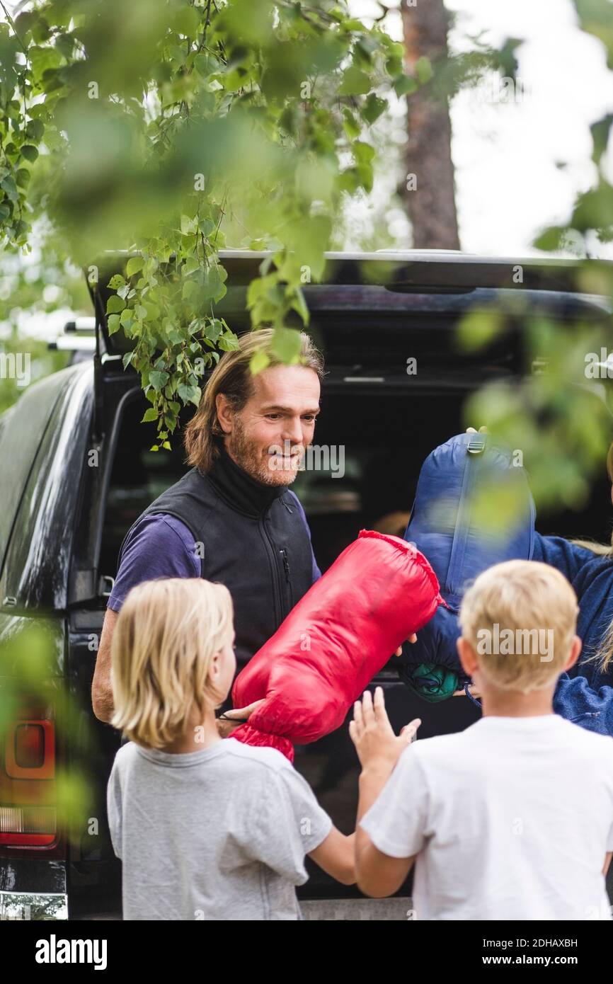 Sorridente padre che dà i bagagli ai bambini mentre scaricano dall'auto Foto Stock