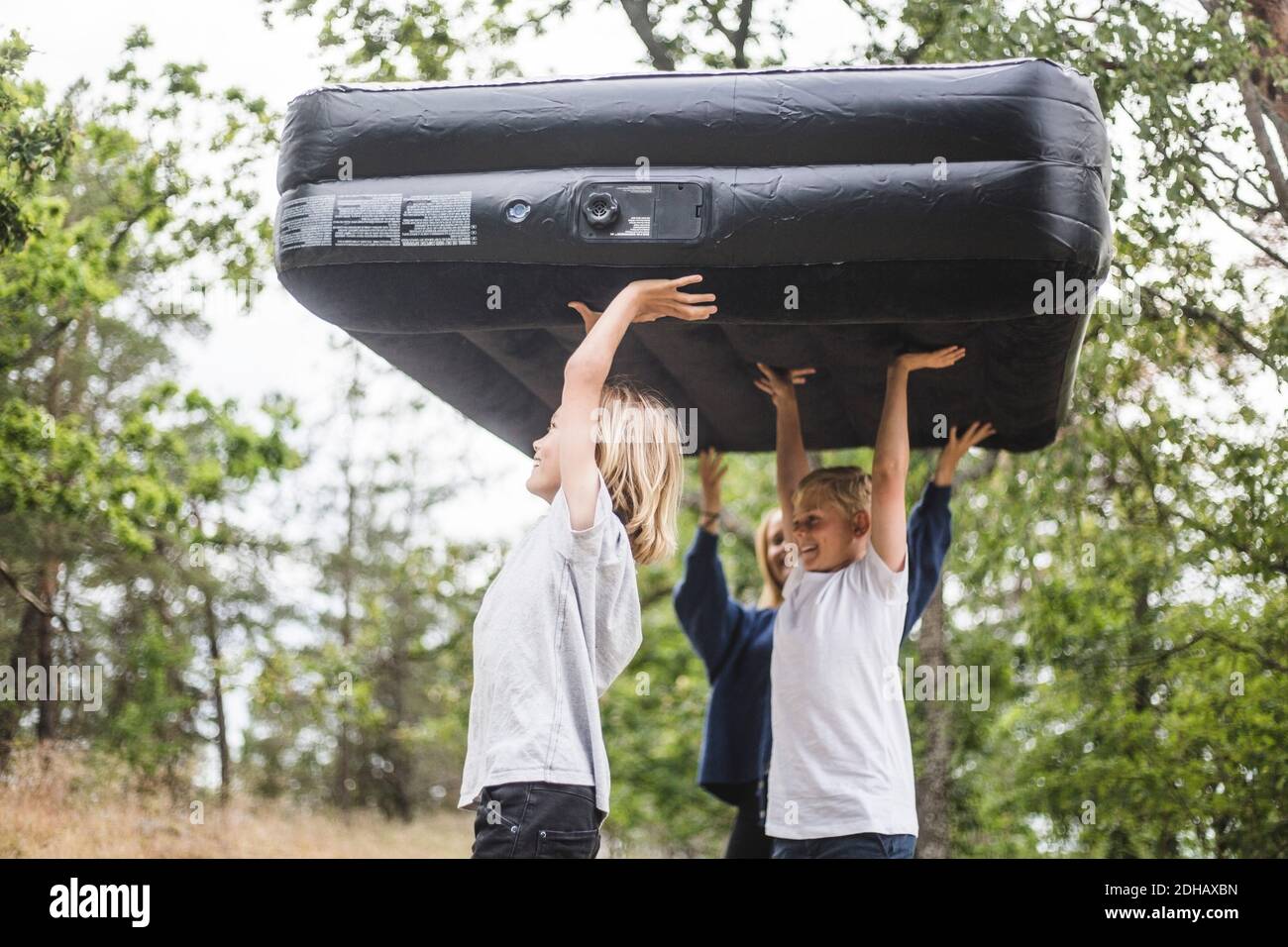 Fratelli che trasportano il materasso gonfiabile che cammina al campeggio Foto Stock