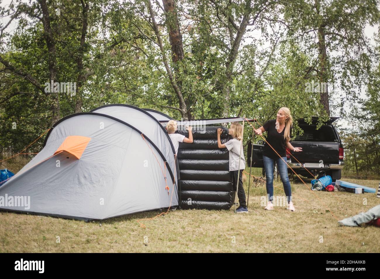 Madre che parla con i bambini che trasportano il materasso nella tenda al campeggio sito Foto Stock