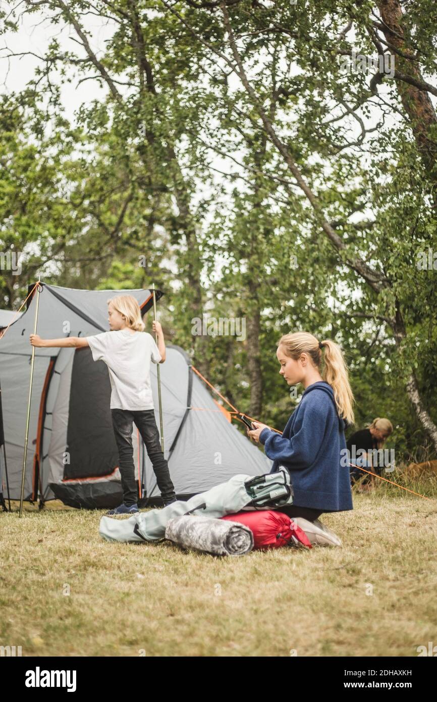 Ragazza adolescente che usa il telefono mentre la famiglia pitching tenda al campeggio sito Foto Stock