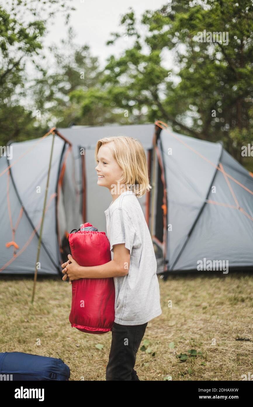 Vista laterale del ragazzo sorridente che tiene la tenda mentre si sta in piedi contro tenda Foto Stock