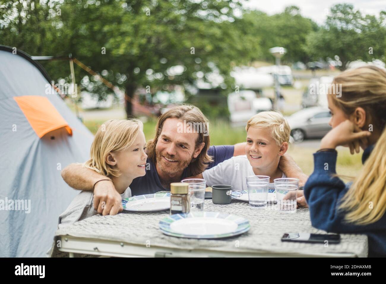 Sorridente padre seduto con i bambini al tavolo in campeggio Foto Stock