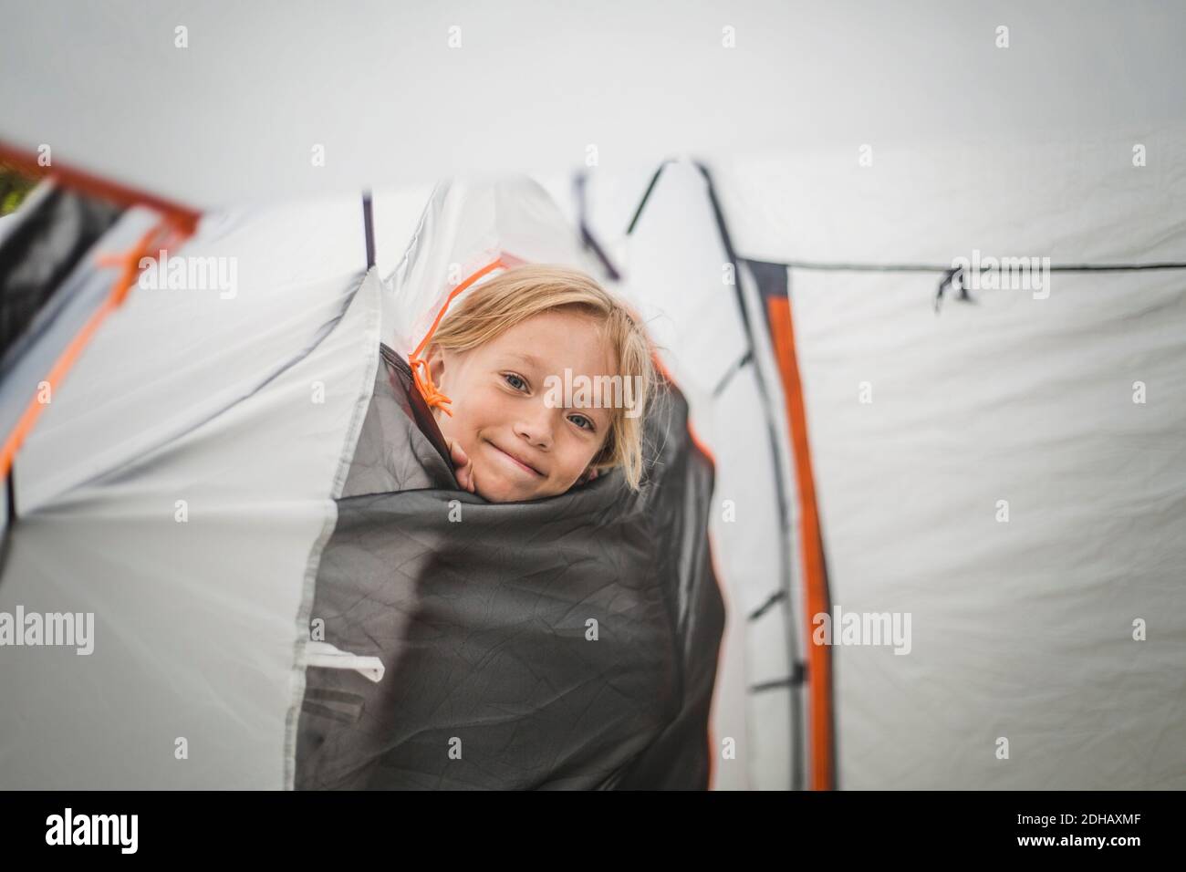 Ritratto di ragazza sorridente che sbirciava attraverso la tenda al campeggio Foto Stock