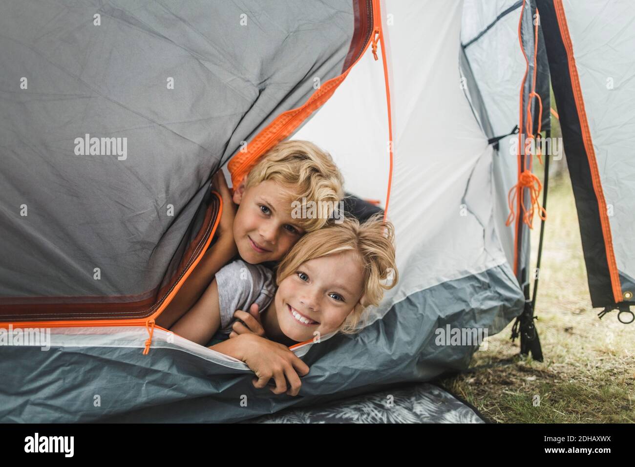 Ritratto di fratelli sorridenti che sbirciano attraverso la tenda al campeggio Foto Stock