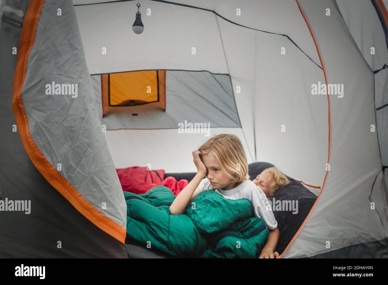 Ragazza sfregando gli occhi mentre si sveglia da fratello in tenda durante il campeggio Foto Stock