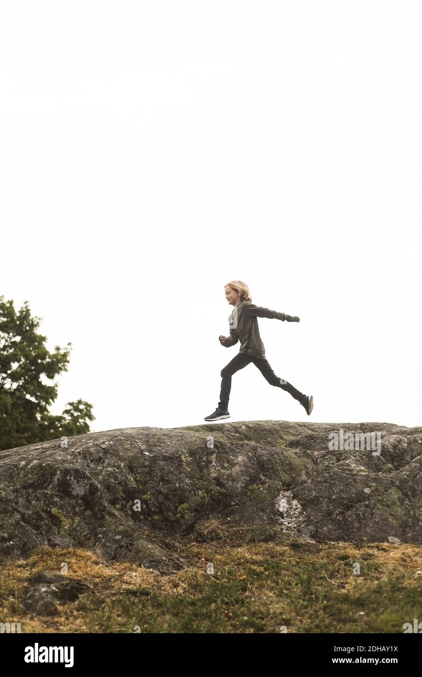 Vista laterale completa della ragazza che corre sulla formazione rocciosa contro il cielo limpido Foto Stock