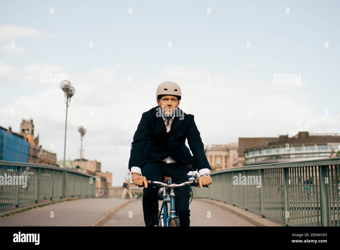 Uomo d'affari sicuro che corre in bicicletta sul ponte in città contro il cielo Foto Stock