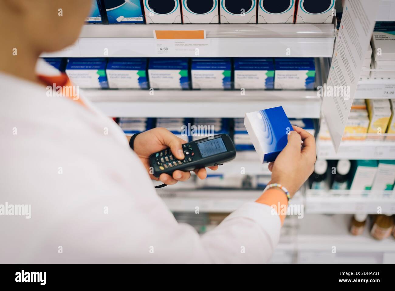 Midsection del farmacista di sesso maschile usando il lettore di codice a barre sul medicinale in piedi in un rack al negozio Foto Stock