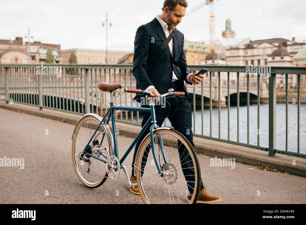 Uomo d'affari sicuro che usa lo smartphone mentre cammina con la bicicletta ponte in città Foto Stock