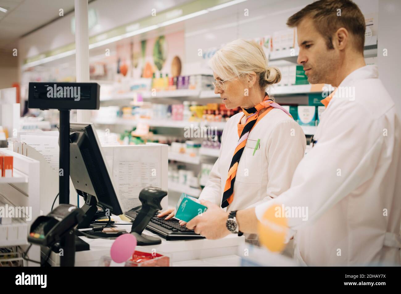 Farmaco di scansione di un farmacista di sesso maschile sicuro con lettore di codici a barre vicino collega di sesso femminile che utilizza il computer al momento del check-out in negozio Foto Stock