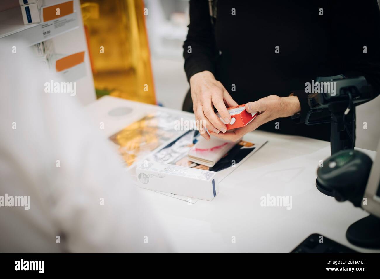 Mezza sezione del cliente anziano che tiene la medicina di prescrizione con il proprietario femminile al momento del check-out in farmacia Foto Stock