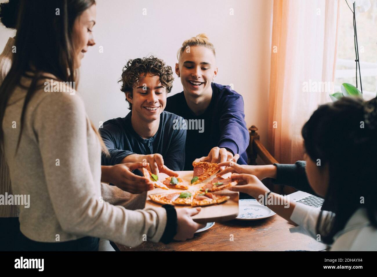 Teenage girl serve pizza ad amici felici al tavolo da pranzo Foto Stock