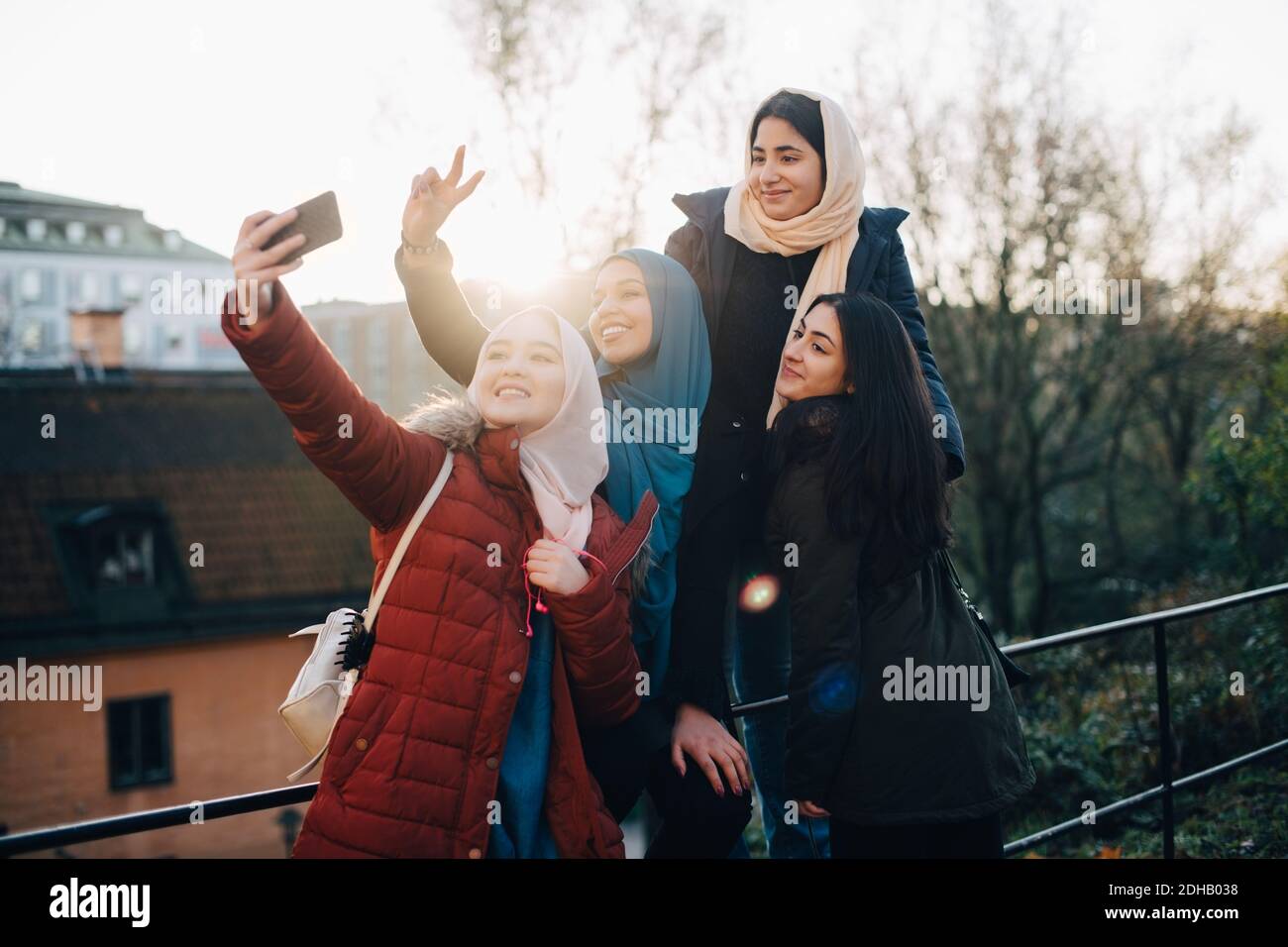 Felice giovane donna musulmana che prende selfie con gli amici tramite ringhiera in città Foto Stock
