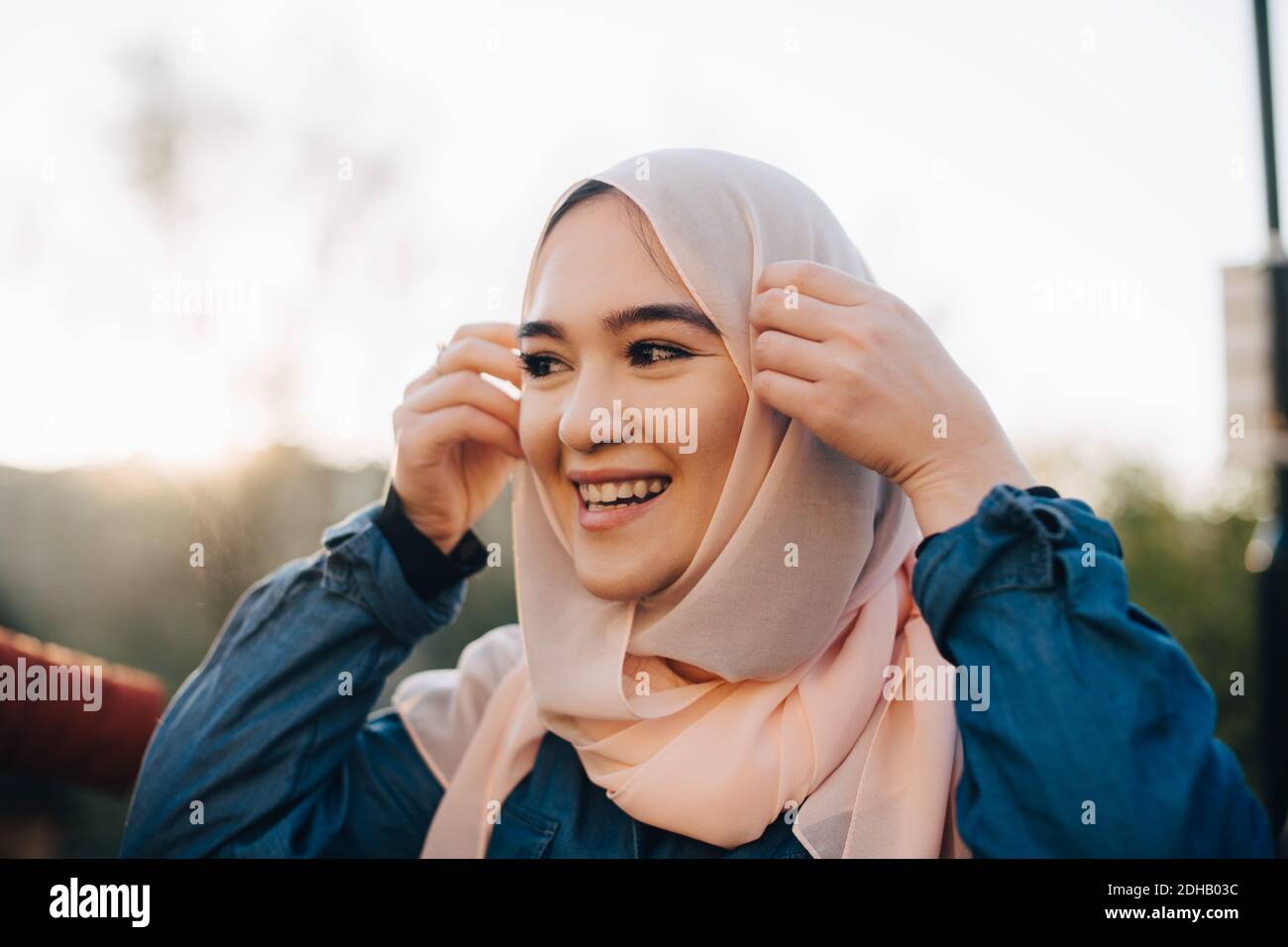 Sorridente giovane musulmana che si adegua hijab contro il cielo limpido Foto Stock
