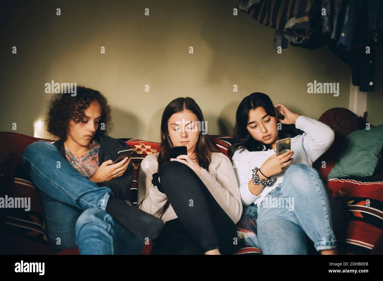 Distratti gli amici di sesso maschile e femminile utilizzando i telefoni cellulari mentre si è seduti sul divano a casa Foto Stock